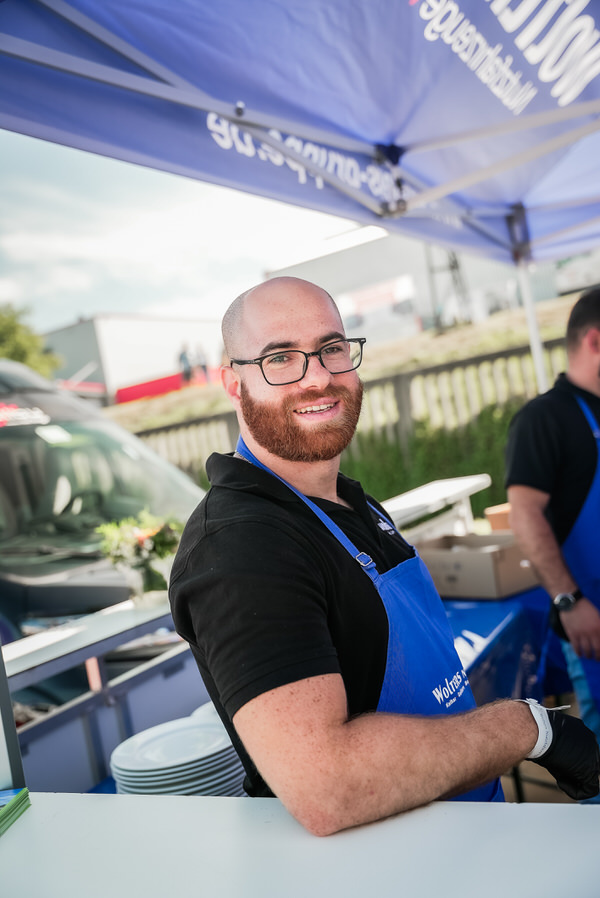 Ein Mitarbeiter mit Vollbart steht an der Essenstheke zur Ausgabe