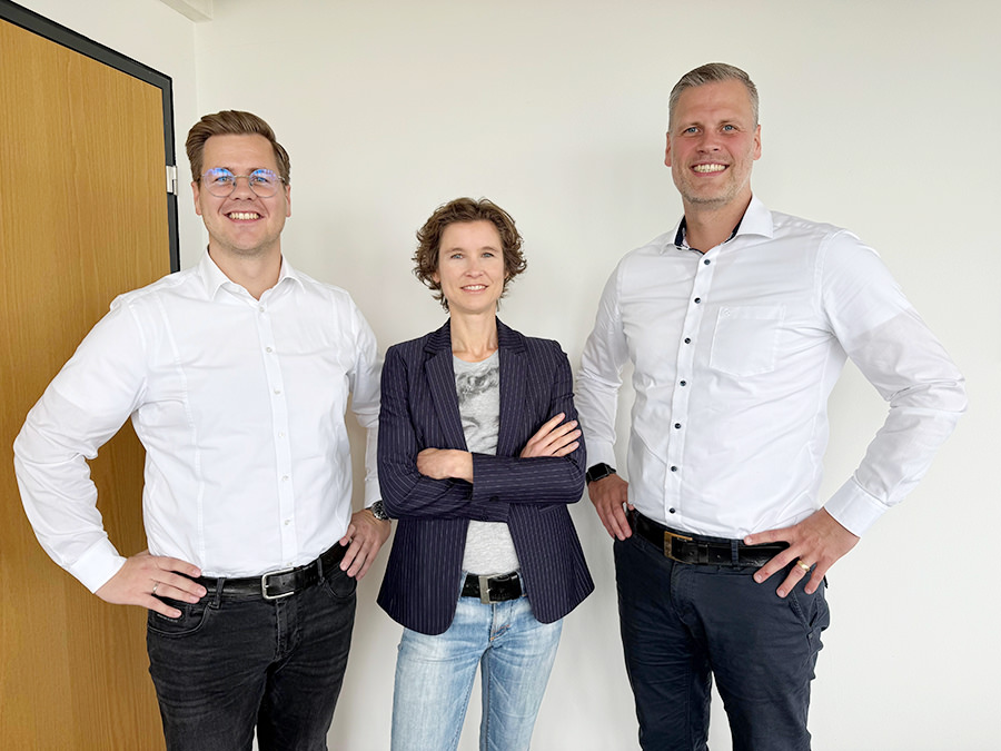 Zwei Männer stehen zusammen mit einer Frau in der Mitte im Büro